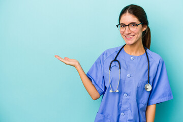Young caucasian nurse isolated on blue background showing a copy space on a palm and holding another hand on waist.