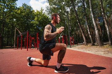 Athletic bearded man doing lunges on sportsground