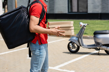 Cropped view of courier with thermo backpack holding boxes with pizza near blurred scooter outdoors