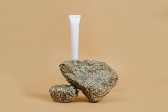 White tube with a cosmic day, night cream for eays with a stone on a beige background. Stylish look of the product, mock up, without a brand.