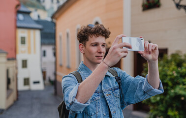 Young man outdoors on trip in town, taking photograph with smartphone.