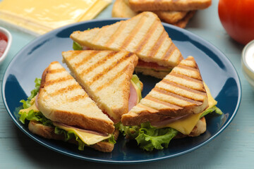 Sandwich on a plate with ham, cheese and tomato on a blue background.