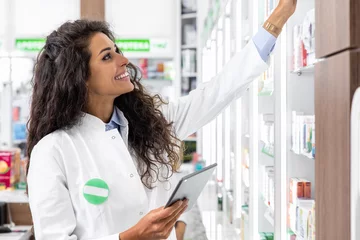 Deurstickers Female pharmacist working in pharmacy using digital tablet during inventory. © Zoran Zeremski