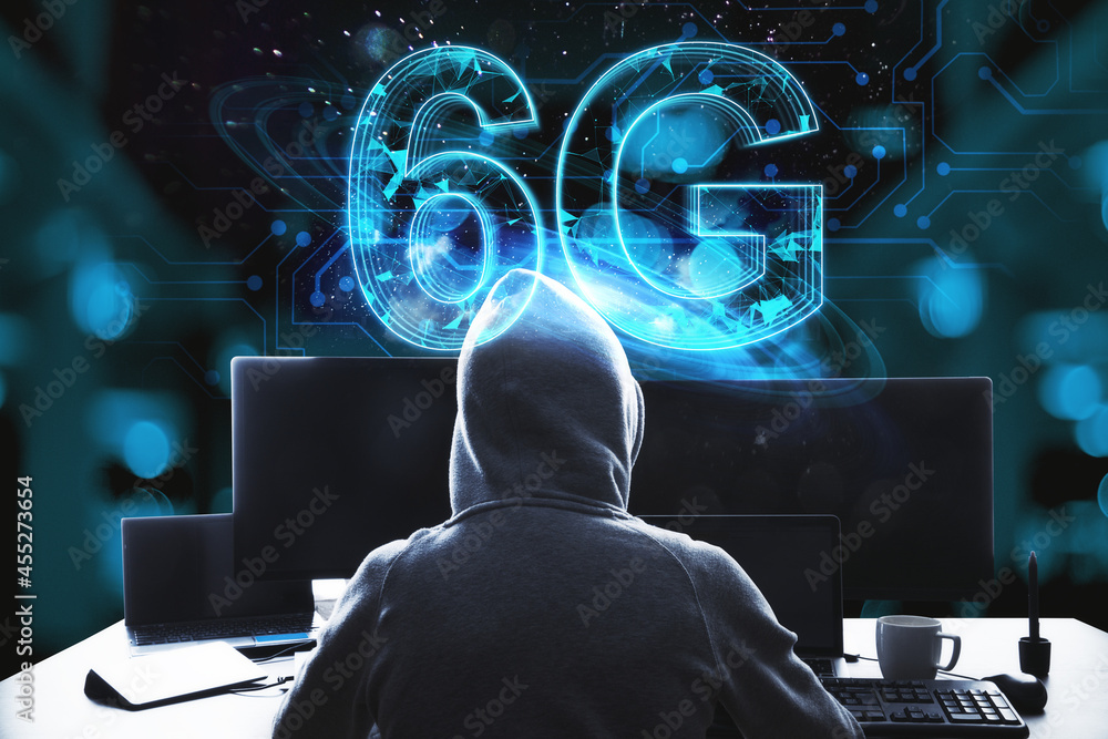 Poster Back view of hacker at desktop using computers with glowing blue 6G hologram on blurry bokeh interior background. Internet speed, theft, hacking and future technology concept.