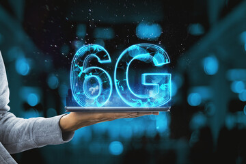 Close up of hand holding tablet with glowing blue 6G hologram on blurry bokeh interior background. Internet speed and future technology concept.