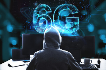 Back view of hacker at desktop using computers with glowing blue 6G hologram on blurry bokeh interior background. Internet speed, theft, hacking and future technology concept.