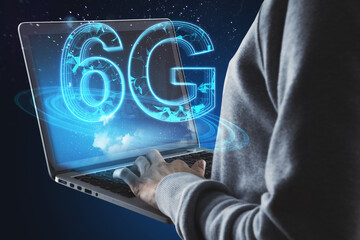 Hacker hands holding laptop with glowing blue 6G hologram on blurry bokeh interior background....