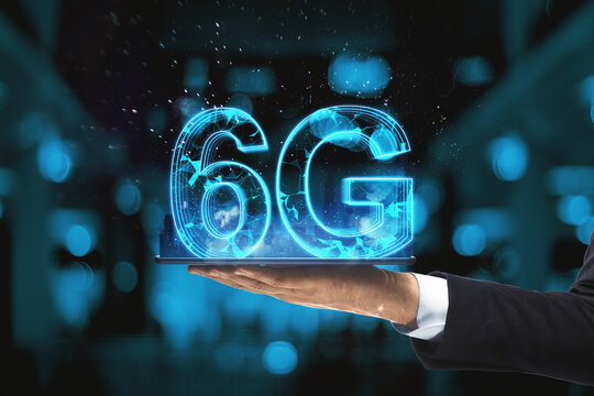 Close up of male hand holding tablet with glowing blue 6G hologram on blurry bokeh interior background. Internet speed and future technology concept.