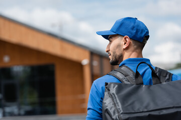 Side view of muslim deliveryman in uniform with thermo backpack outdoors - obrazy, fototapety, plakaty