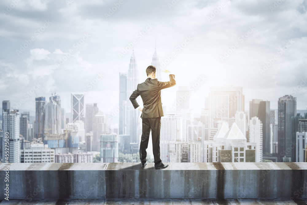 Poster back view of young business man standing on concrete edge of building on city background with mock u