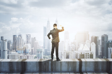 Back view of young business man standing on concrete edge of building on city background with mock...