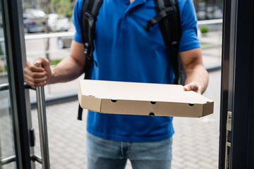 Cropped view of pizza box in hand of blurred courier near door