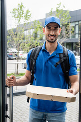 Cheerful muslim deliveryman holding pizza box near door