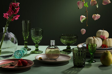 Beautiful table decorated with green and mini pumpkins in plate, flower bouquets in tall vases and served with porcelain plates and green glasses. 