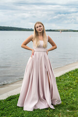 Fototapeta na wymiar Young woman enjoying summer time posing alone in cute ping dress near lake
