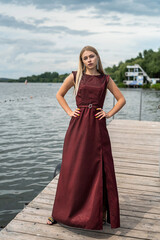 Fototapeta na wymiar Beautiful girl in long fashionable dark red dress near pond in sity park