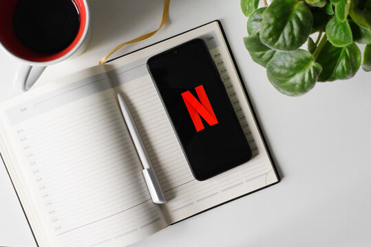 Netflix logo on smartphone screen top view, mobile application streaming video service, sign of an American entertainment company. Mobile phone, diary, coffee cup and home plant in the workplace