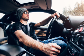 Adult man in hat and glasses driving a sports car