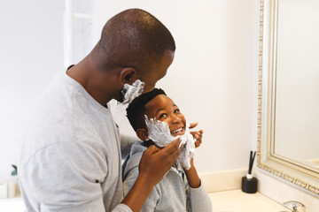 African american father with son having fun with shaving foam in bathroom