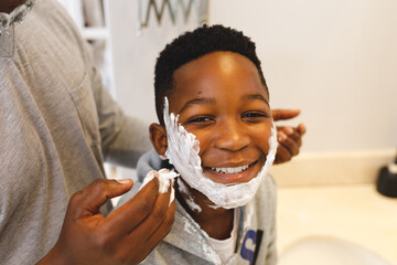 Portrait of african american son having fun with father and shaving foam in bathroom