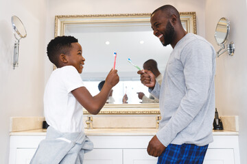 African american father with son having fun and brushing teeth in bathroom
