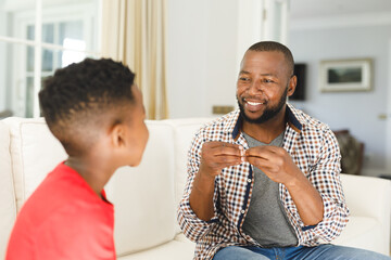 Happy african american father with son sitting on couch in living room talking sign language