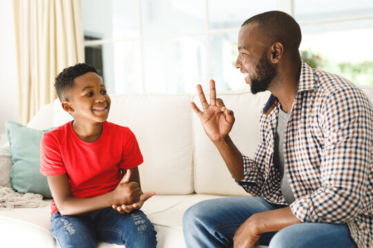 Happy african american father with son sitting on couch in living room talking sign language