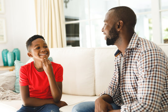 Happy african american father with son sitting on couch in living room talking sign language
