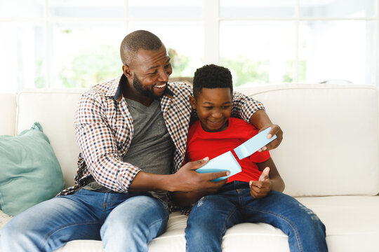 Happy african american father opening gift from his son and smiling in living room