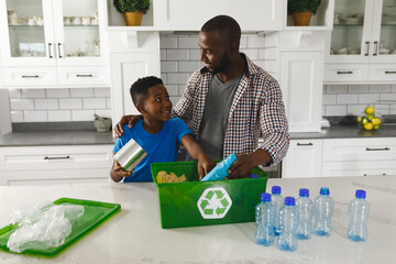 Happy african american father and son in kitchen talking and sorting rubbish for recycling - Powered by Adobe