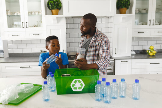 Happy african american father and son in kitchen talking and sorting plastic waste for recycling - Powered by Adobe