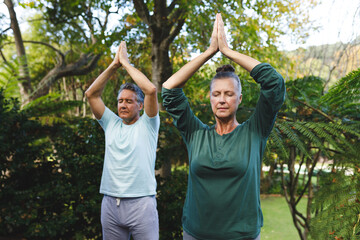 Happy senior caucasian couple practicing yoga, meditating in sunny garden