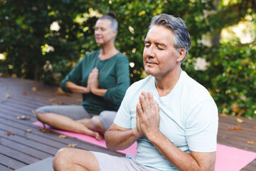 Obraz premium Happy senior caucasian couple practicing yoga, meditating in sunny garden