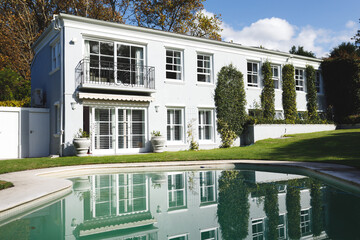 Large house with swimming pool and trees in sunny garden