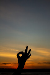 Silhouette of a man's hand during sunset making the OK symbol.