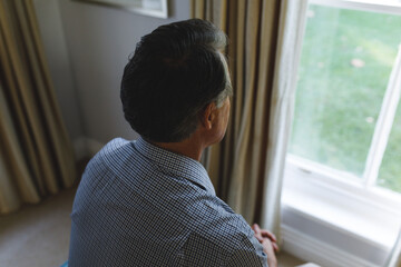 Thoughtful senior caucasian man sitting on sofa and looking through window