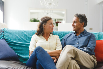 Happy senior caucasian couple in living room sitting on sofa, talking