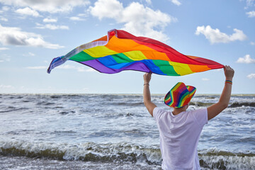 Man standing by the sea and holding the LGBTQ pride flag. LGBTQ concept