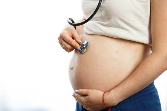 Pregnant woman with stethoscope trying to hear her baby heartbeat at home. Woman with tammy preparing for the birth of the baby.