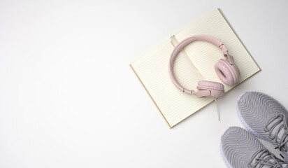 pink wireless headphones, a pair of sneakers and a notepad on a white background, top view. Womens clothing