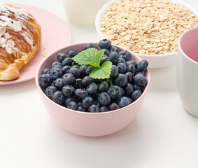 ripe blueberries in a pink ceramic plate on a white table, breakfast ingredients