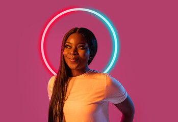 Portrait of african happy young girl in neon light on dark studio background with neoned blue circle. Concept of youth, music, disco, ad, sales