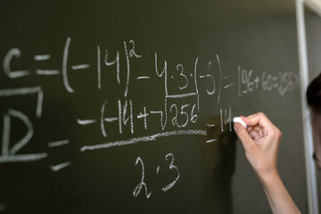 female hand writing math formulas on the classboard