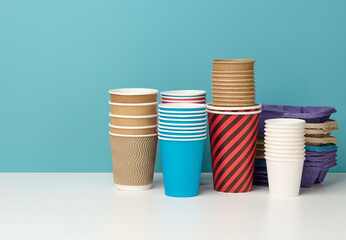 stack of paper disposable multi-colored cups and stand on white table, blue background