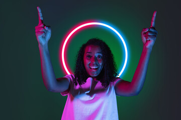 Portrait of african happy smiling girl in neon light on dark studio background with neoned blue circle. Concept of youth, music, disco, ad, sales