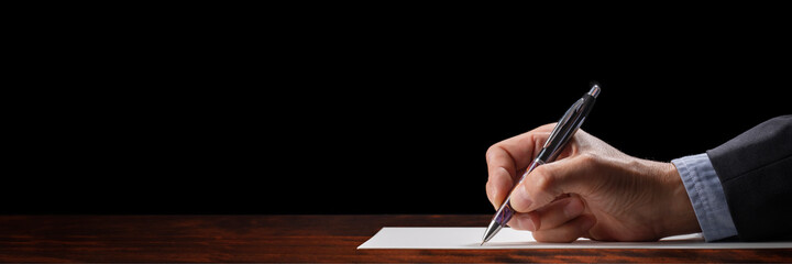 白い紙に、ペンで字を書いている手。もしくは書類にサインをしている手
