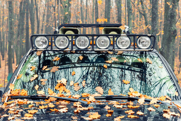 Close-up detail view of custom made roof rack bar with extra headlight mounted on roof of heavy duty pick up suv car against foggy autumn forest. Fallen leaves vehicle windshield. Fall weather drive
