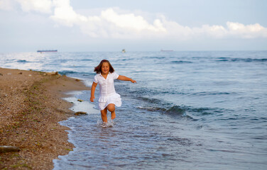 Fototapeta na wymiar Child tanned girl running jumping on beach showing freedom