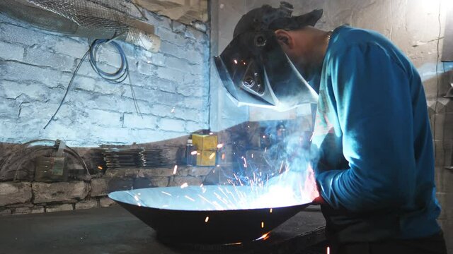 Man welding parts of the metal detail together at industrial manufacture. Worker in protective mask welding metal construction at metalworking production. Welder doing joint between two steel details