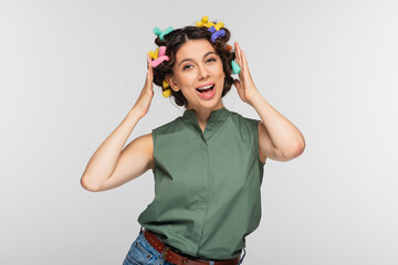 amazed young woman with colorful hair curlers isolated on grey